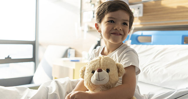 Close up of beautiful little boy hugging his teddy bear while looking away daydreaming and smiling.